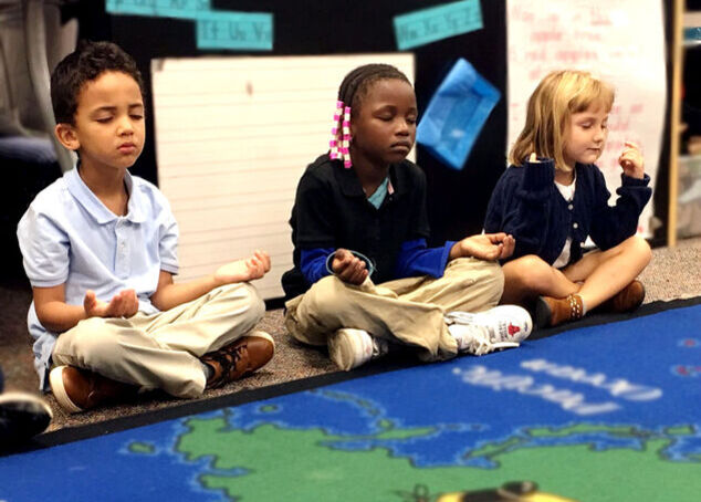 Three students sitting in a meditative pose listening to Mindful Music Moments.